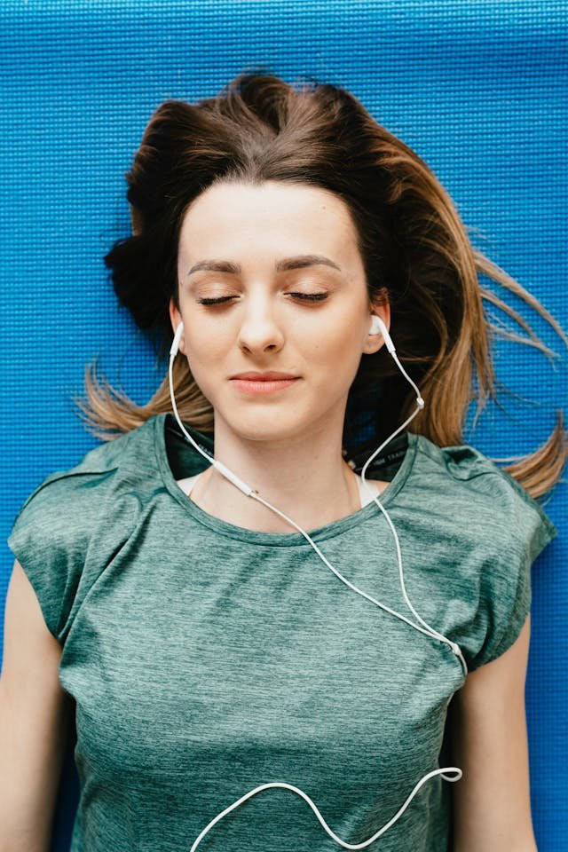 a woman lying on a blue mat with headphones on her ear