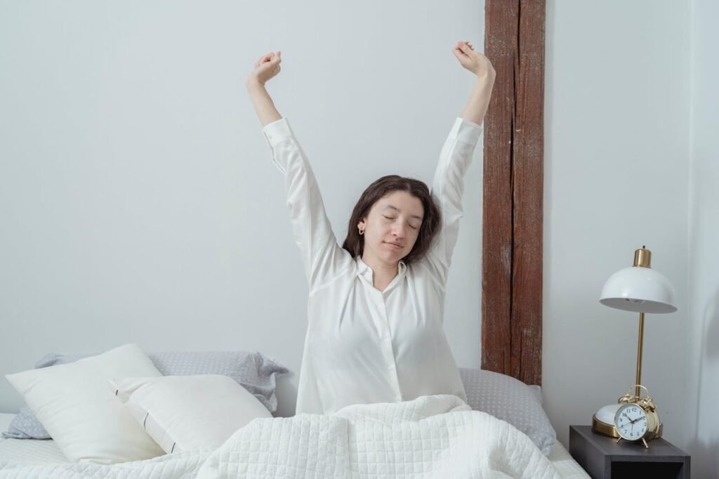 A serene morning scene in a cozy bedroom, sunlight streaming through the window and casting a warm glow across the rumpled bedsheets. On the nightstand, an alarm clock displays the time, a silent reminder to abandon the temptation of the snooze button. In the foreground, a hand reaches towards the alarm, hesitating, as the sleeper contemplates breaking free from the alluring comfort of the bed. The scene evokes a sense of tranquility and the internal struggle to overcome the habit of hitting snooze, capturing the essence of "How to stop using the snooze button." como parar de usar o despertador